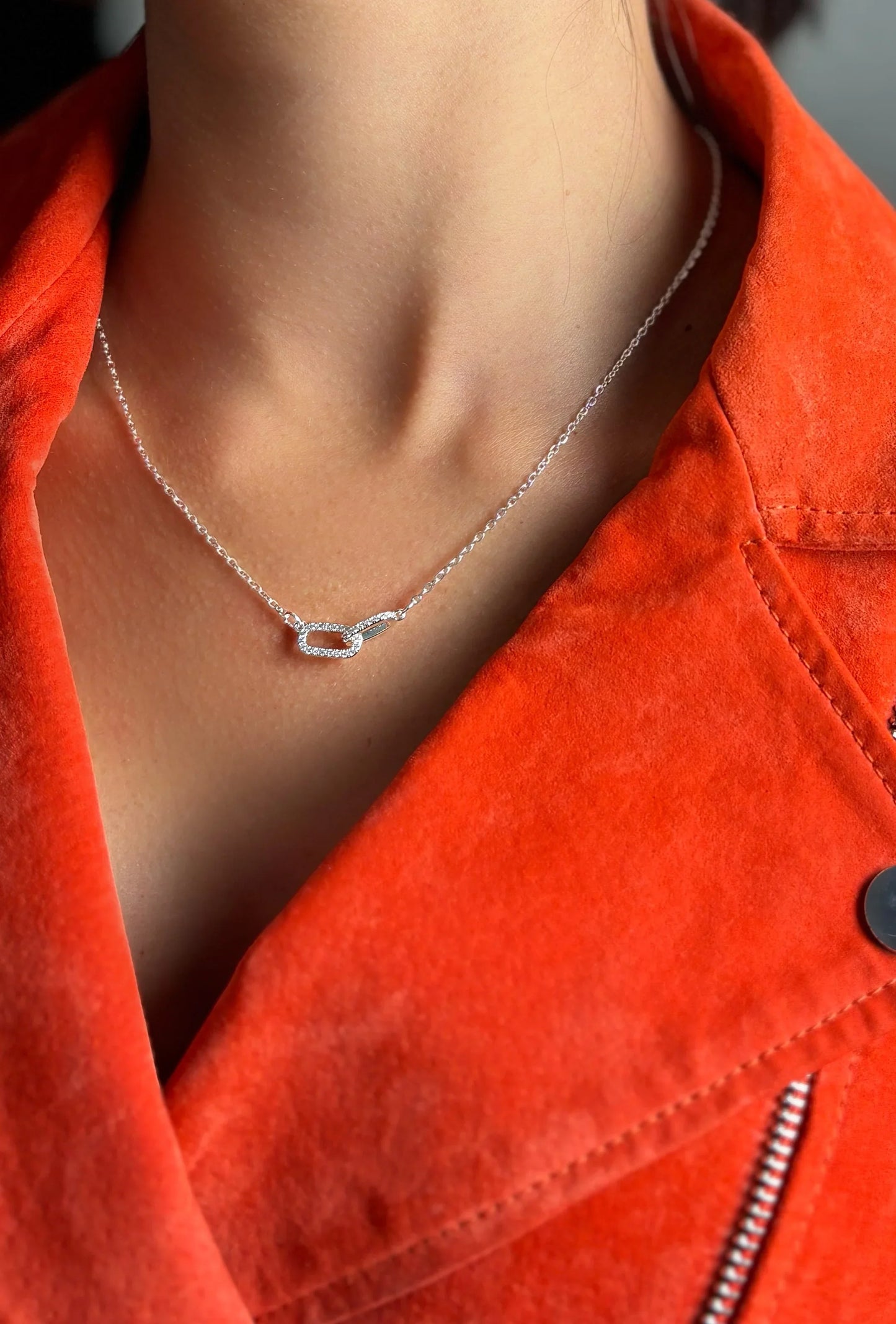 Collar de bisutería fina MYKOANI con dije brillante, sobre chaqueta naranja.