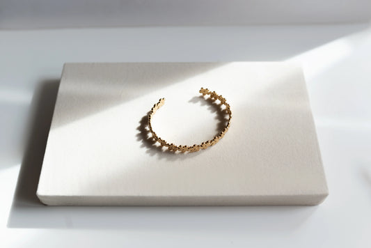 Brazalete dorado de alta bisutería MYKOANI con diseño floral, sobre fondo claro elegante.