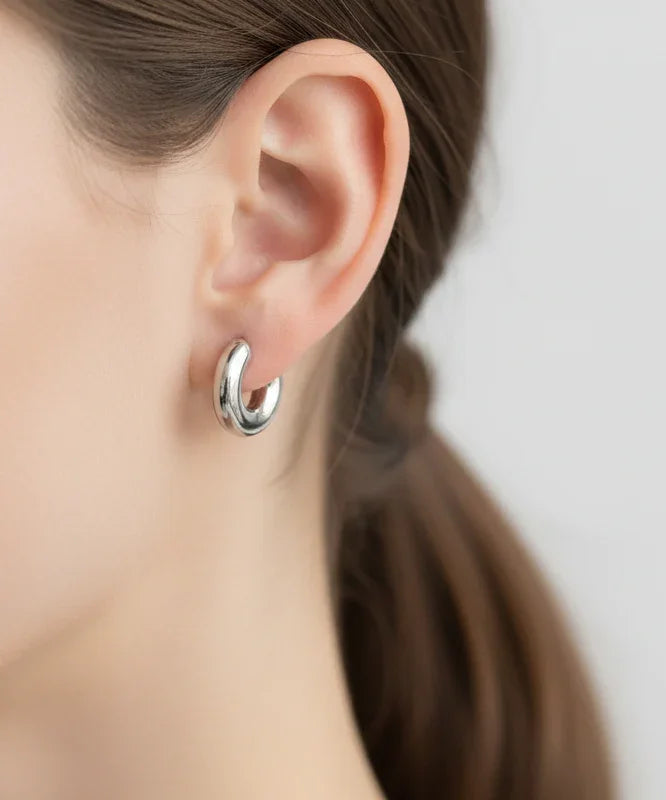 Aro de bisutería fina plateado de MYKOANI puesto en oreja femenina, estilo elegante.