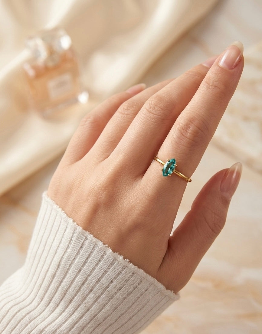 Mano con anillo de bisutería fina dorado y piedra azul, MYKOANI alta bisutería.