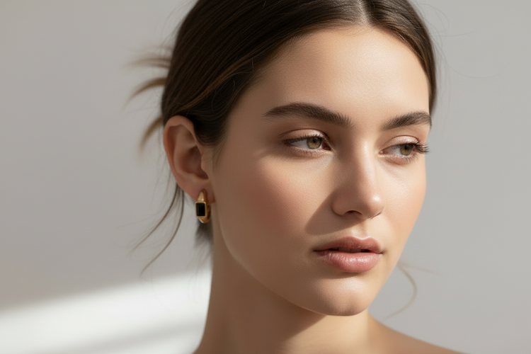 Mujer luciendo arete de bisutería fina dorada con piedra negra, joya exclusiva Mykoani.