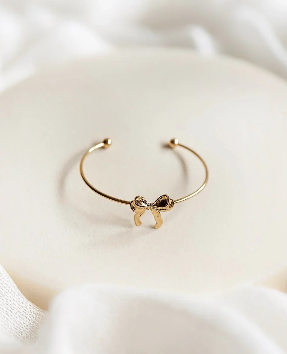 Pulsera de alta bisutería dorada con lazo, diseño exclusivo MYKOANI sobre fondo blanco.
