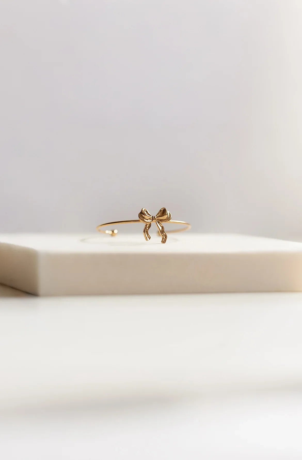 Pulsera fina de bisutería dorada con lazo, diseño exclusivo MYKOANI sobre fondo neutro