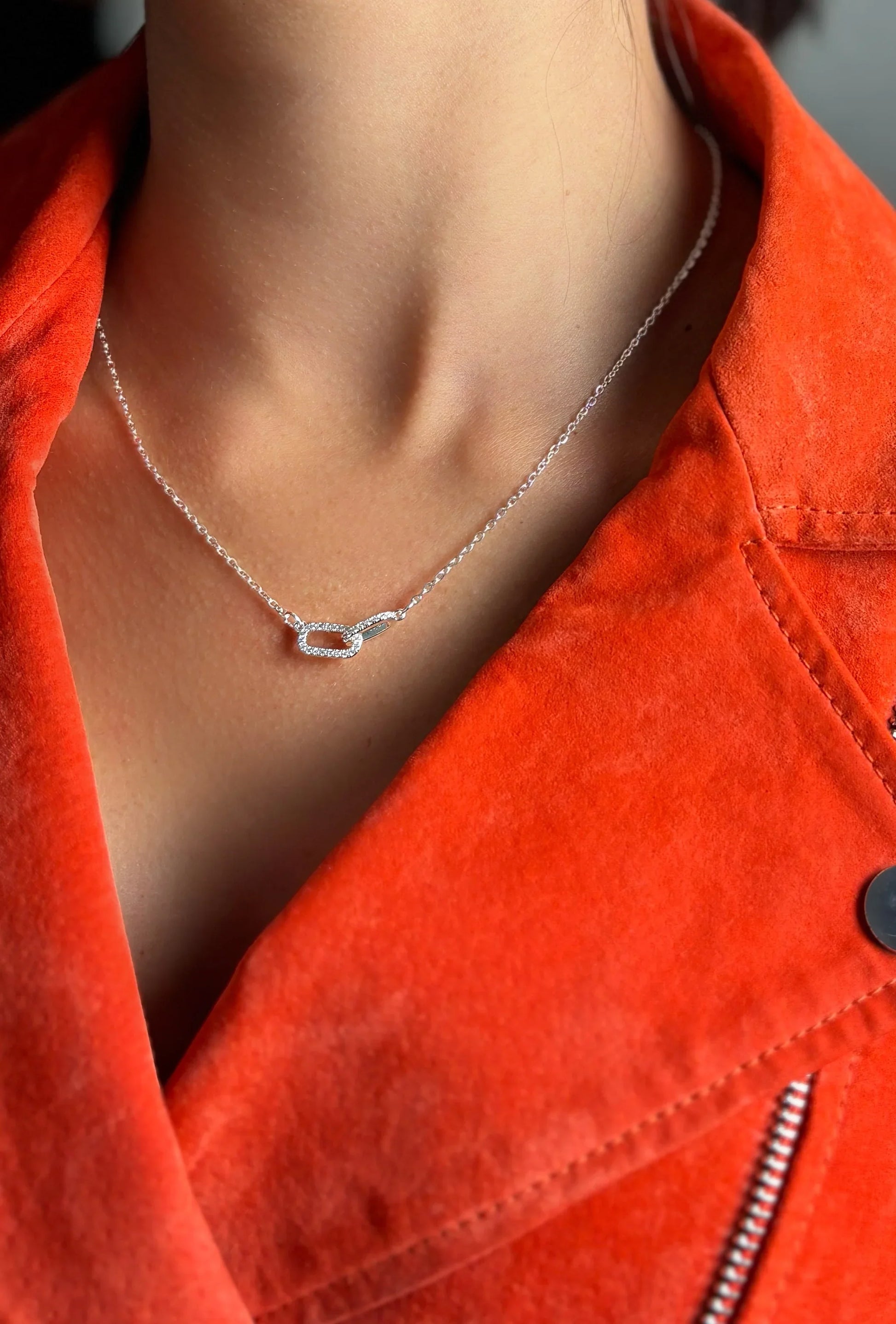 Collar de bisutería fina MYKOANI con dije brillante, sobre chaqueta naranja.