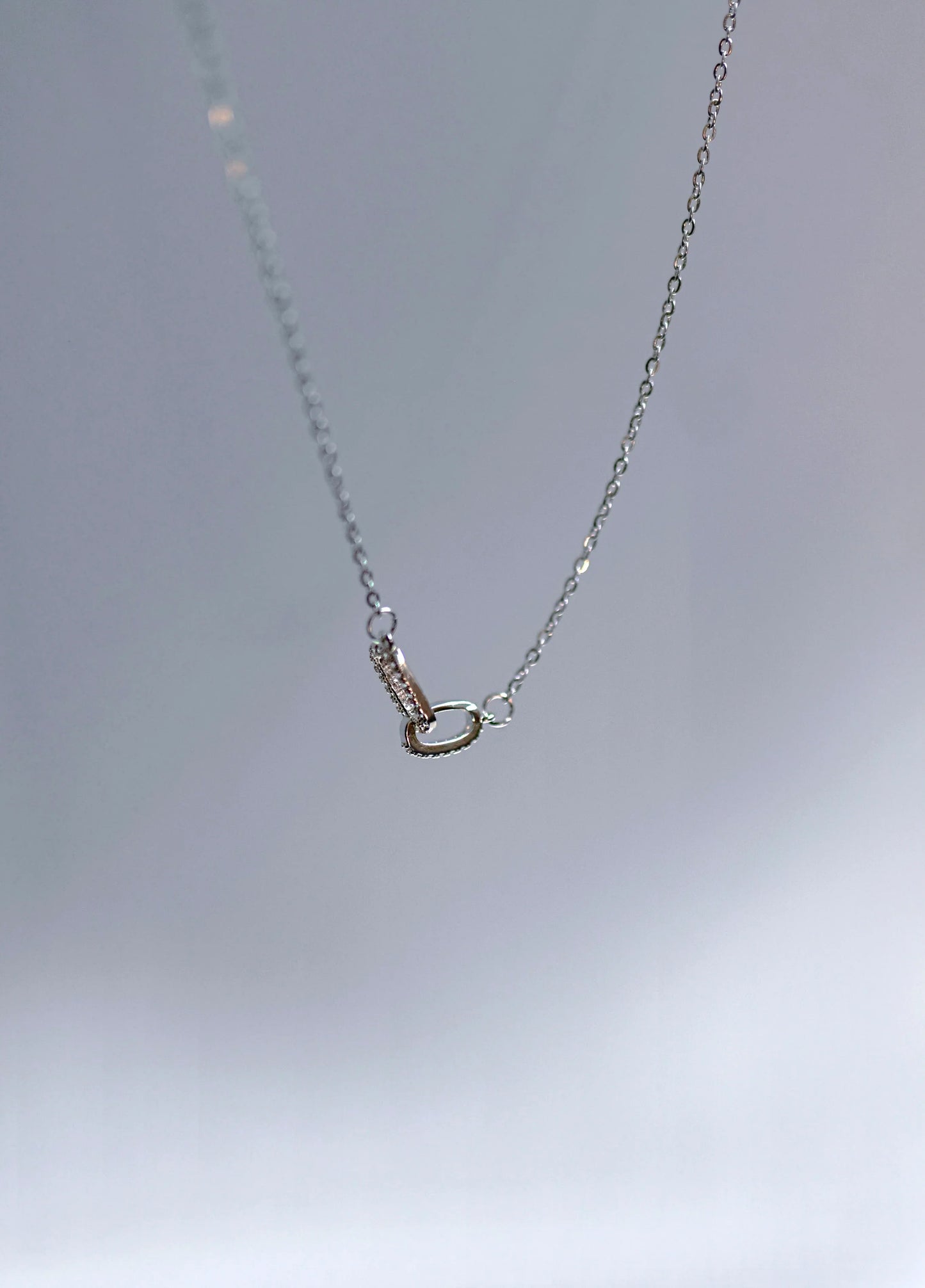 Collar de cadena fina con dije ovalado, bisutería de diseño exclusivo Mykoani sobre fondo gris.