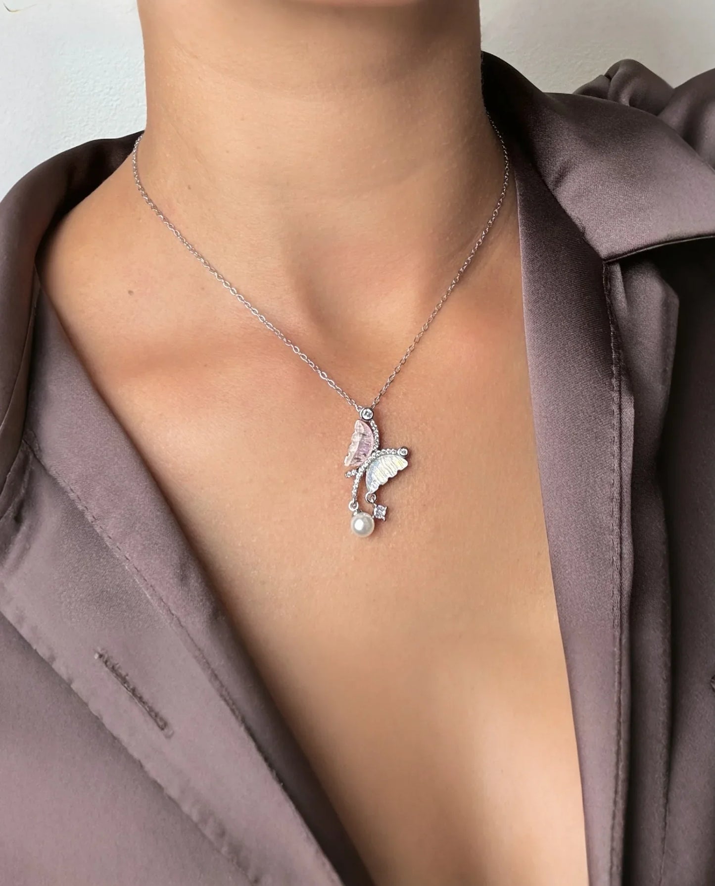 Collar de mariposa con perla, bisutería fina exclusiva MYKOANI sobre blusa satinada lila.