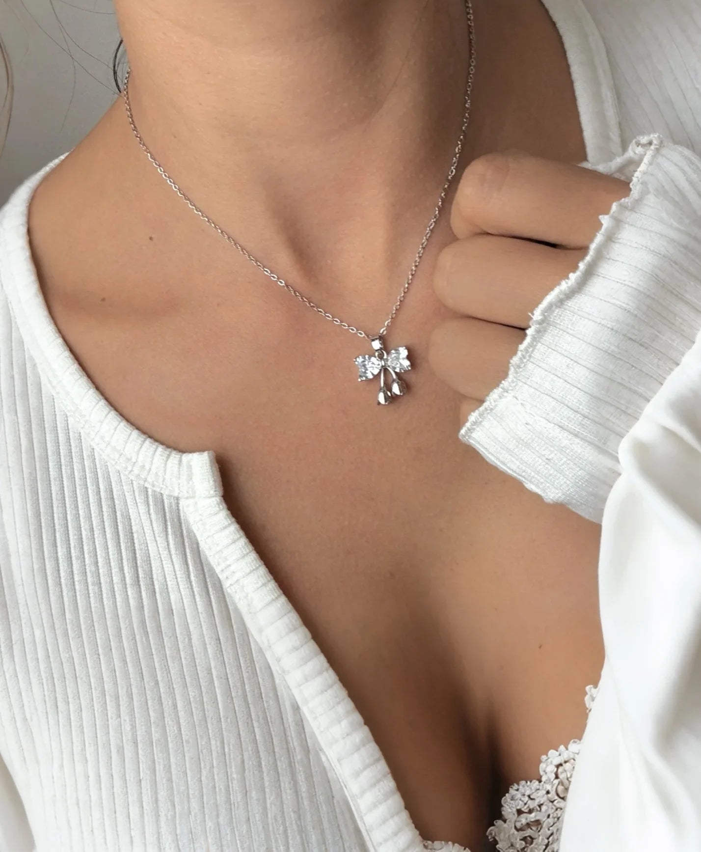 Collar de bisutería fina MYKOANI con dije brillante en forma de lazo sobre blusa blanca elegante.