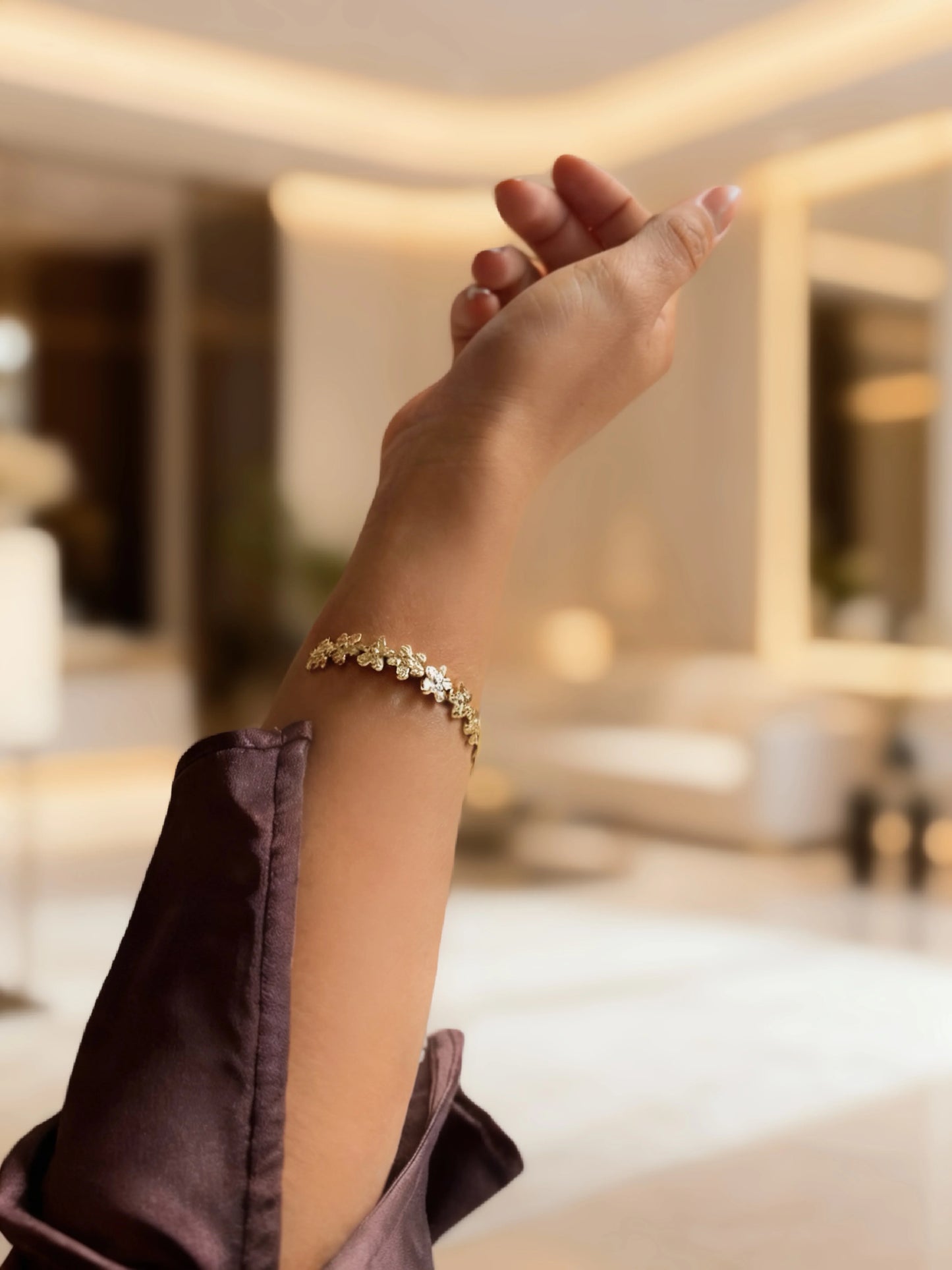 Brazalete de bisutería fina dorado con flores, modelo MYKOANI, en ambiente elegante.