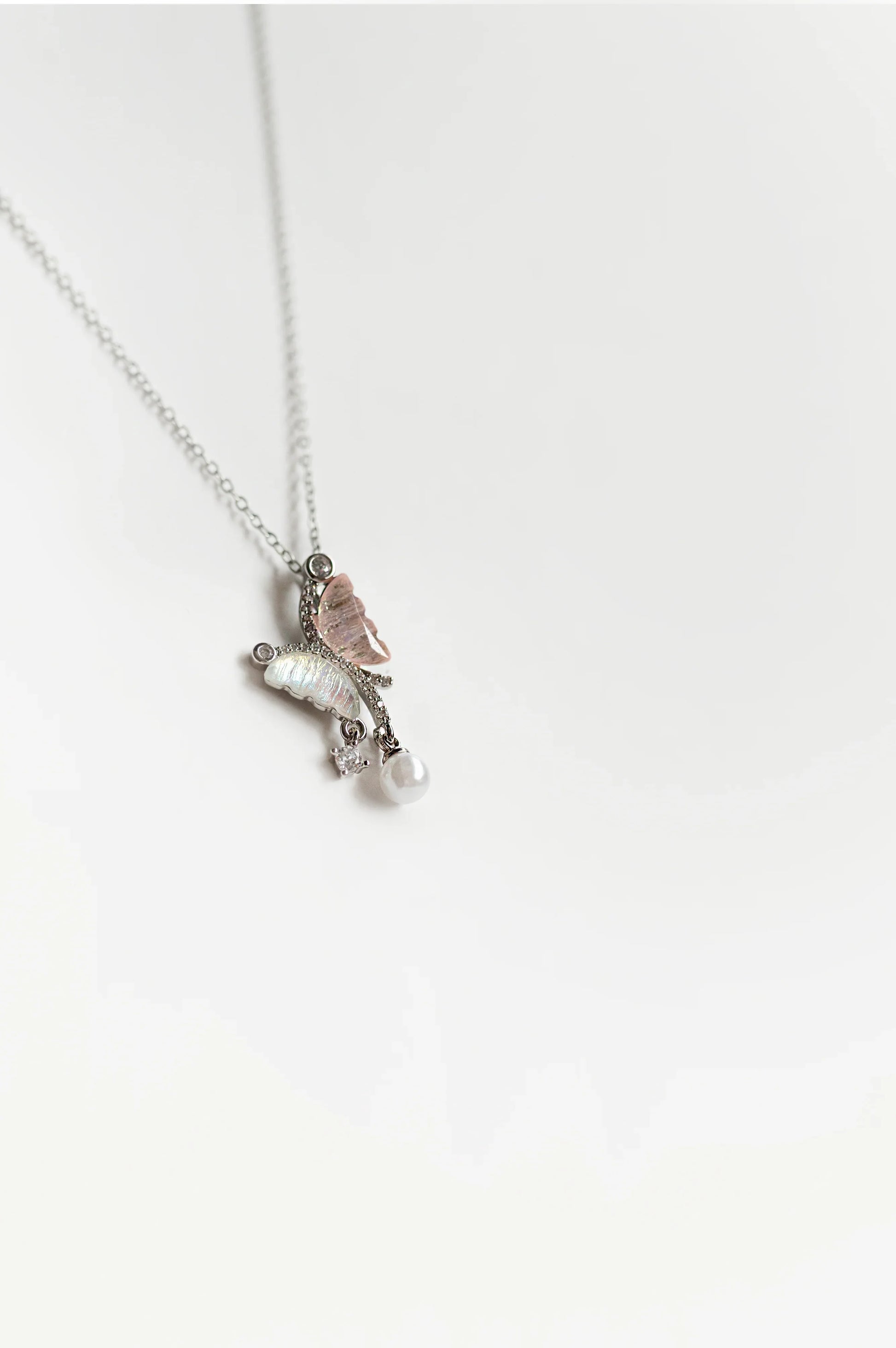 Collar de bisutería fina MYKOANI con dije de mariposa, perla y cristal, fondo blanco elegante.