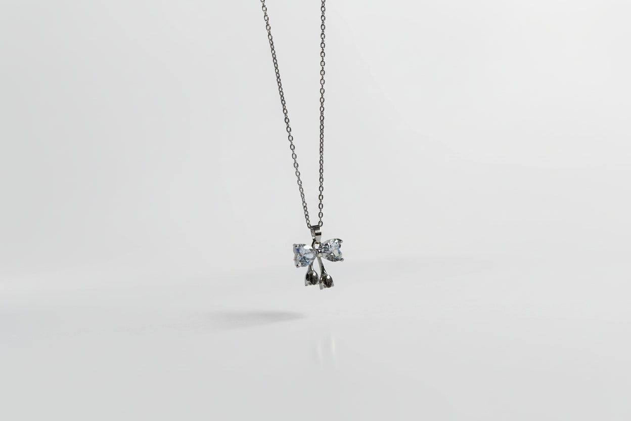 Collar delicado de bisutería fina MYKOANI con dije en forma de lazo y brillantes, fondo blanco.