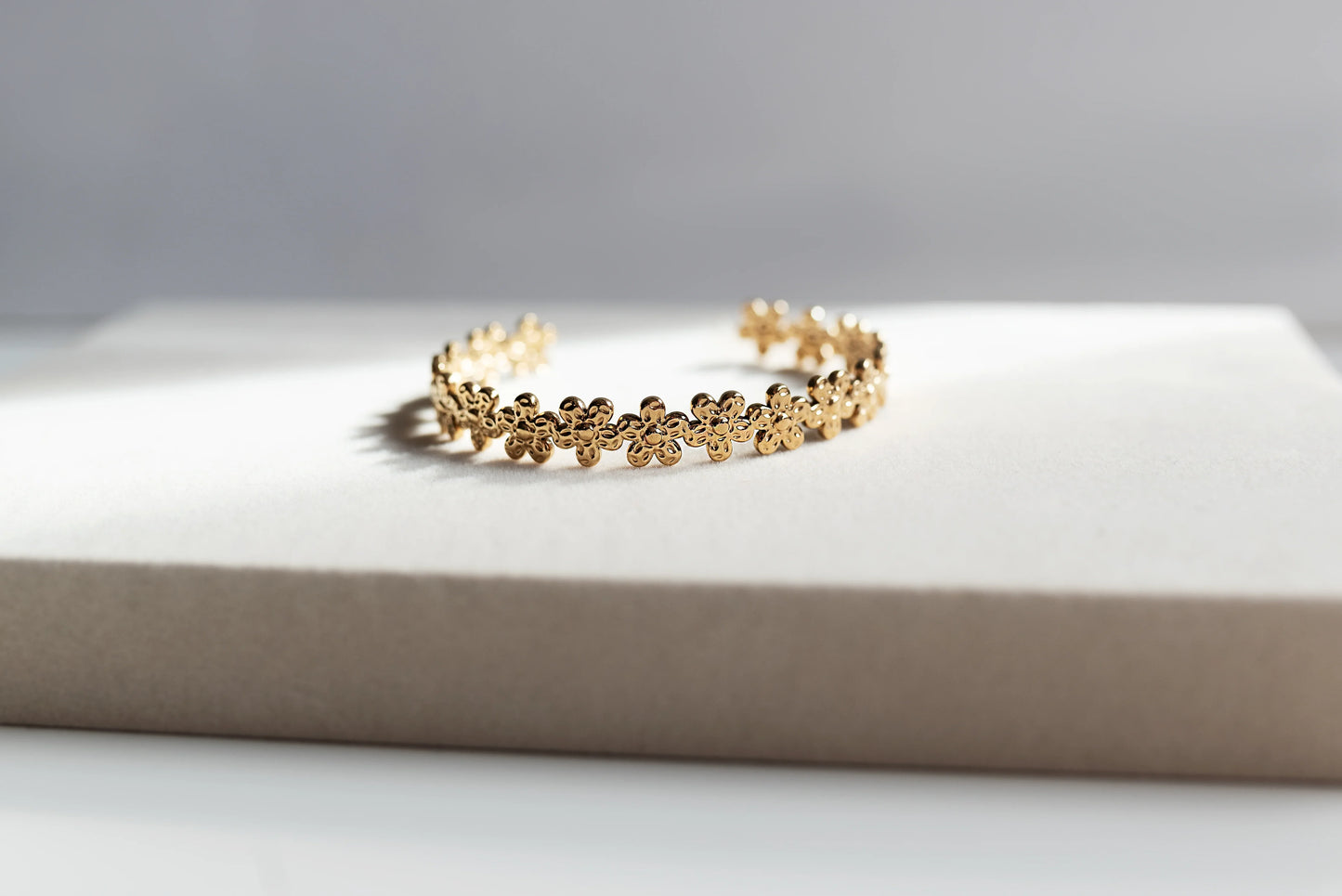 Pulsera dorada de flores, bisutería exclusiva Mykoani, sobre fondo neutro elegante