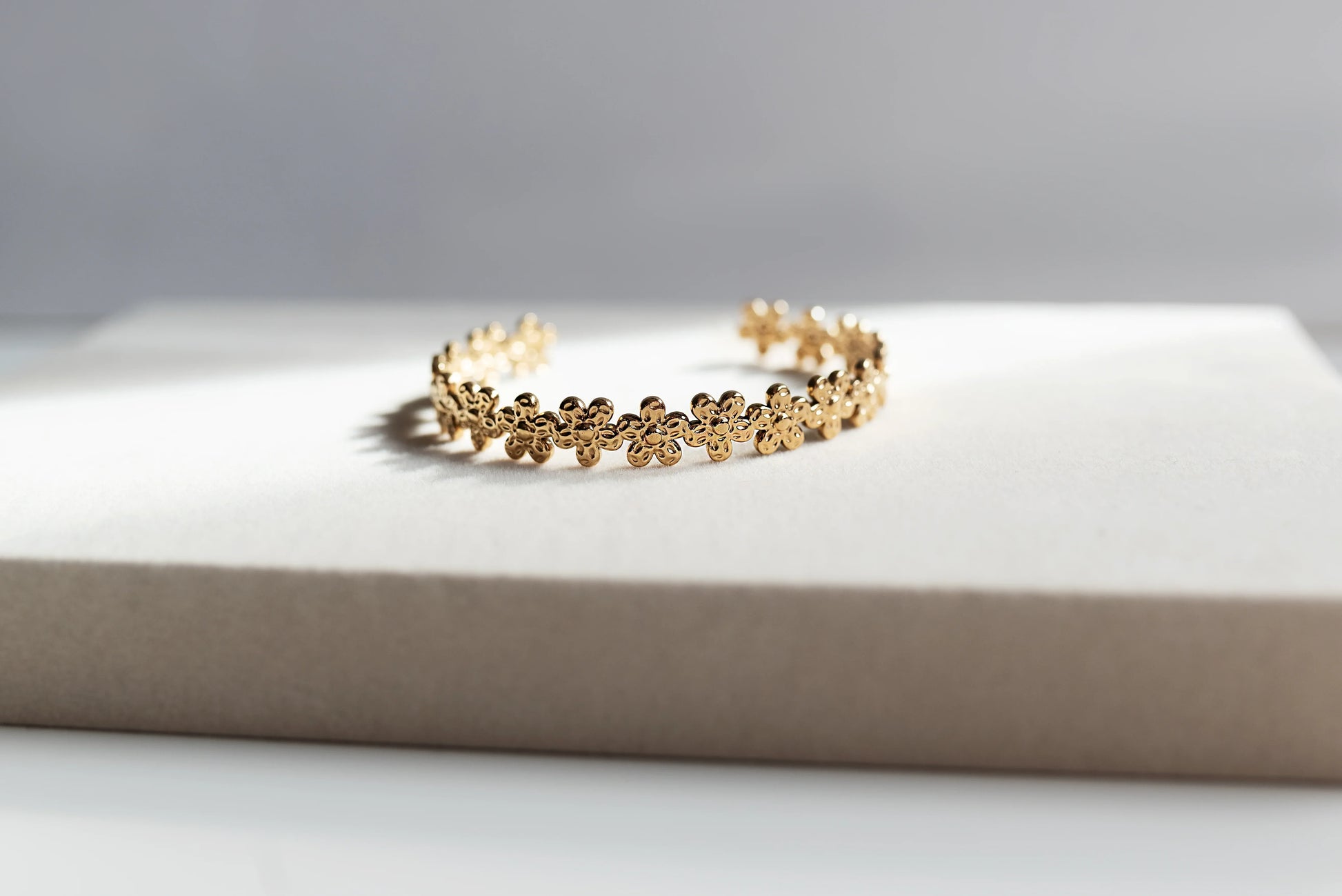 Pulsera dorada de flores, bisutería exclusiva Mykoani, sobre fondo neutro elegante