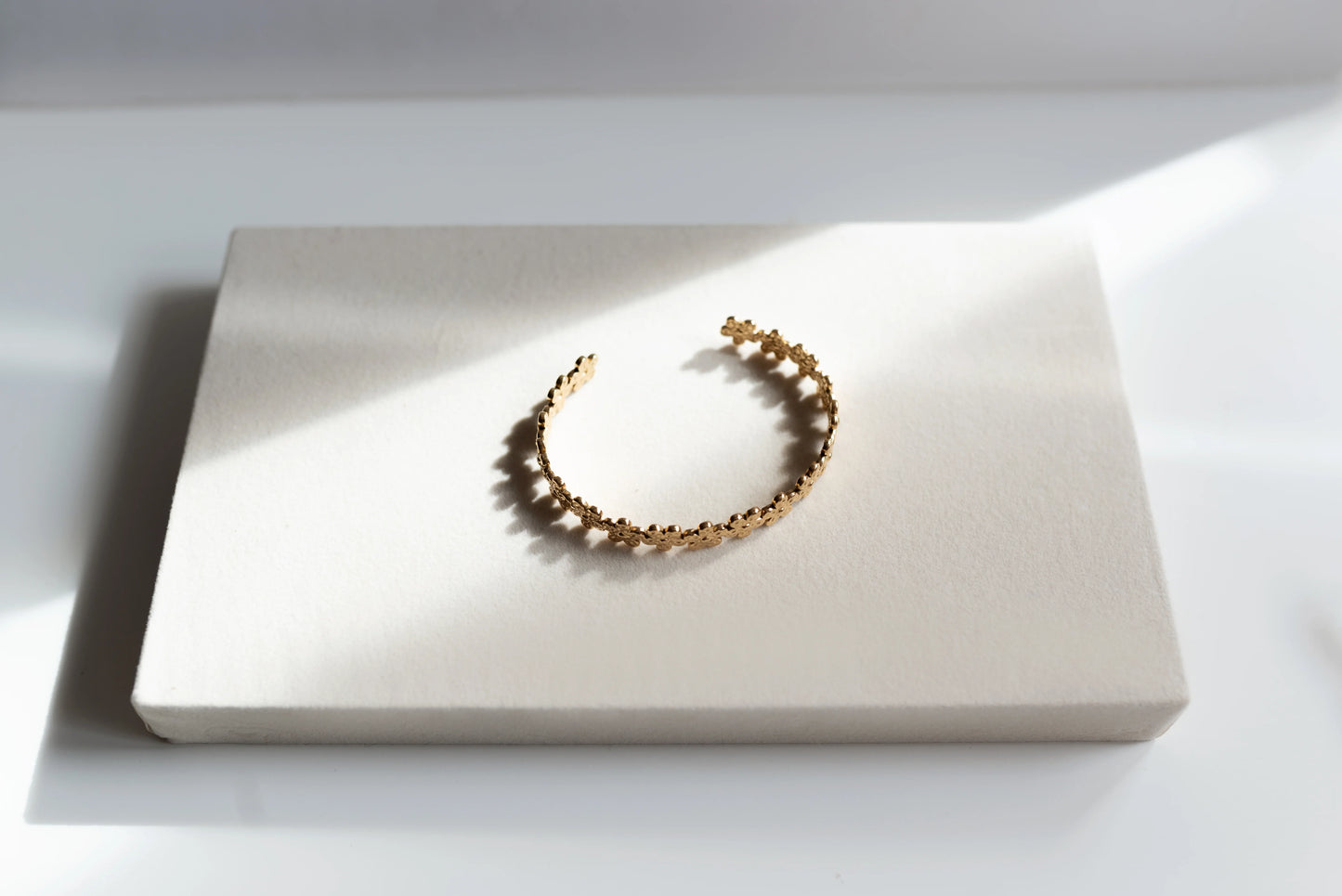 Brazalete dorado de alta bisutería MYKOANI con diseño floral, sobre fondo claro elegante.