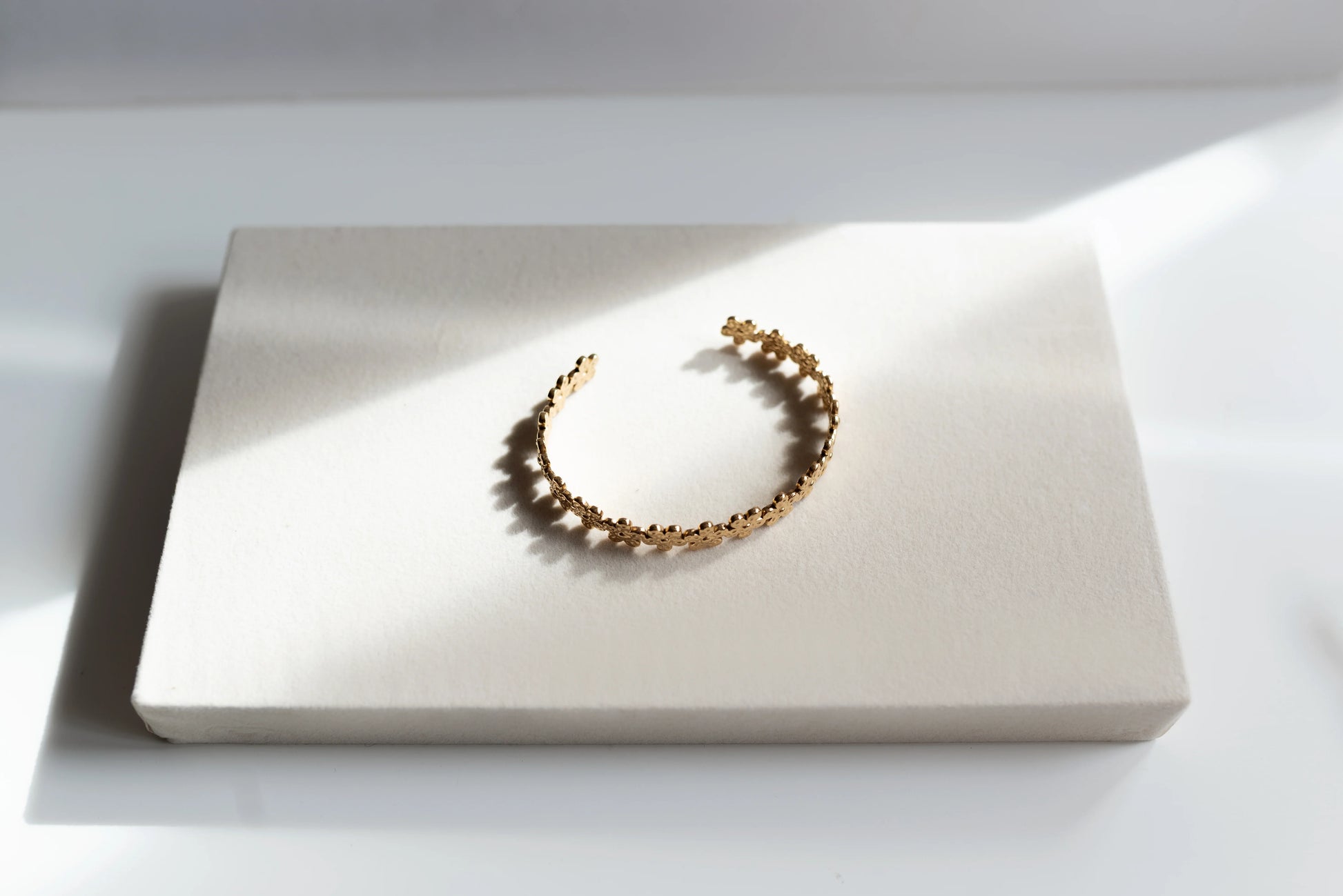 Brazalete dorado de alta bisutería MYKOANI con diseño floral, sobre fondo claro elegante.