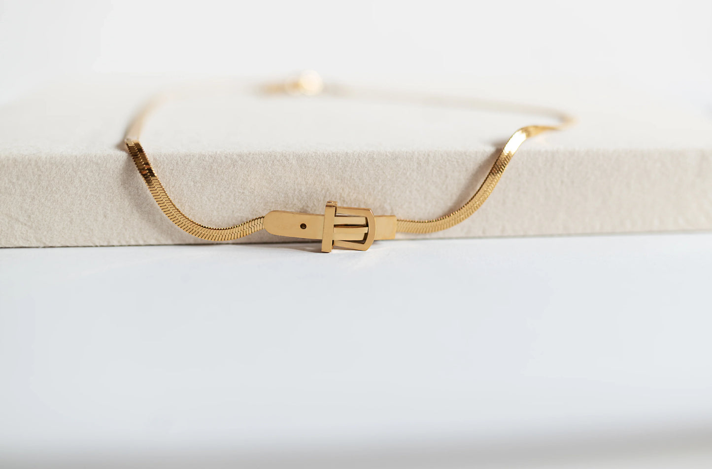 Collar de bisutería fina dorado de MYKOANI con broche distintivo sobre superficie beige