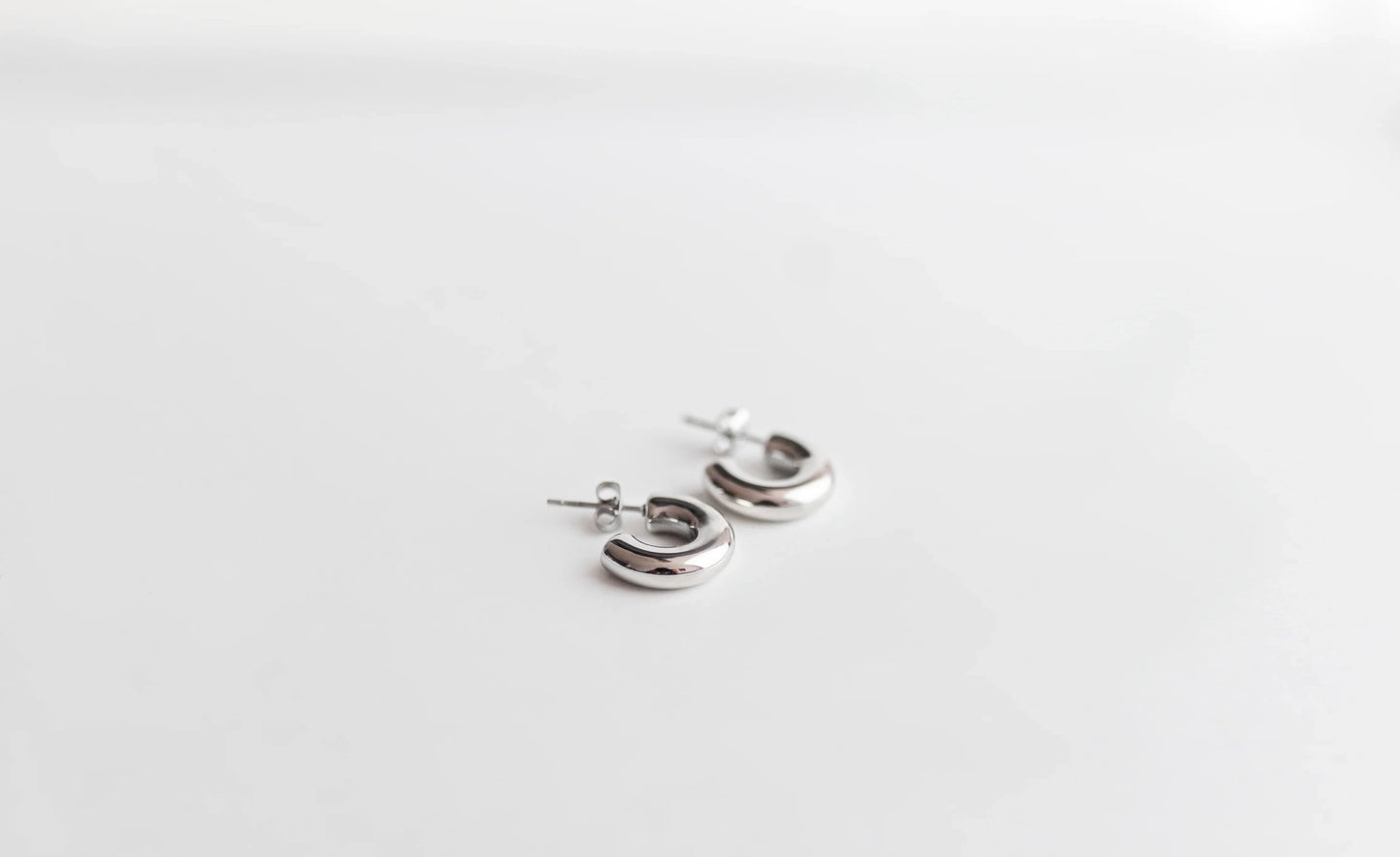 Pendientes de aro pequeños de bisutería fina plateados sobre fondo blanco, MYKOANI