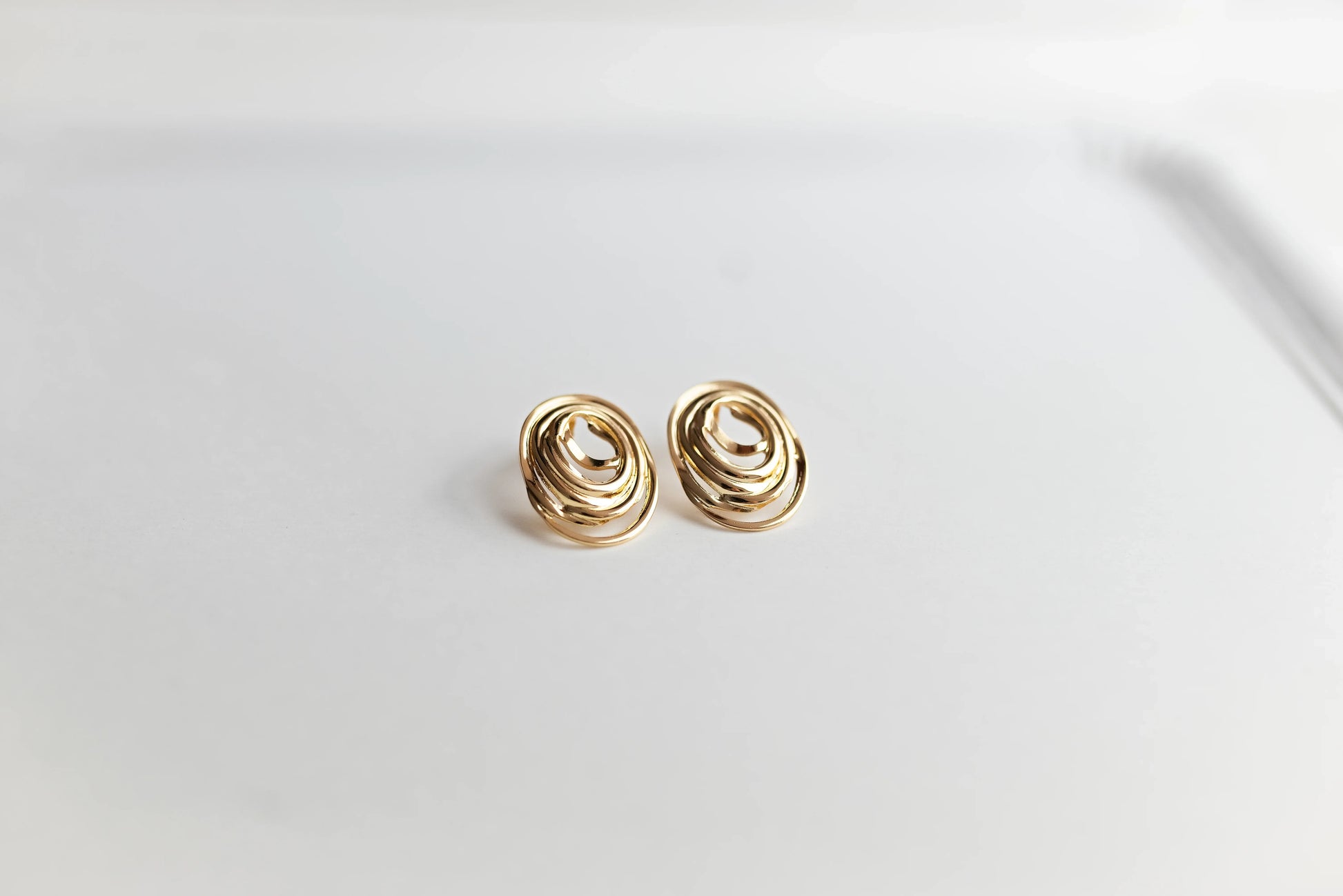Pendientes ovalados dorados de bisutería fina MYKOANI sobre fondo blanco minimalista